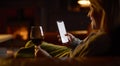 Woman At Home Lying On Sofa In Lounge With Cosy Fire With Blank Screen Mobile Phone Holding Glass Of Wine Royalty Free Stock Photo