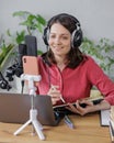 woman in a home office records podcast audio content with a microphone and headphones and a labrador dog