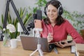 woman in a home office records podcast audio content with a microphone and headphones and a labrador dog