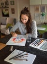 Woman at home at the table, draws paints, portrait of a girl. Bright orange paints, color palette. Black table, brush