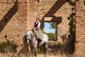 Woman horsewoman, young and beautiful, standing, riding her horse, in the field next to a ruined building. Concept horse riding,