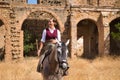 Woman horsewoman, young and beautiful, standing, riding her horse, in the field next to a ruined building. Concept horse riding,