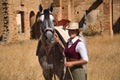 Woman horsewoman, young and beautiful, with stick and hat, next to her horse, in the countryside next to a ruined building.