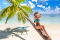 Woman in hot sunny weather laying down on a palm tree and enjoying tropical beach vacation, carefree holiday Royalty Free Stock Photo