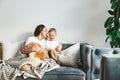 Woman hugging her little son and their dog, sitting on a couch, wrapped in a warm blanket