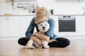 Woman hugging little dog while posing on floor in kitchen Royalty Free Stock Photo