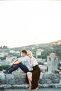 Woman hugs man from behind, resting her head on his shoulder, sitting on a stone fence Royalty Free Stock Photo