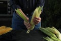 Woman husking corn cob at black table, closeup