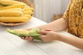 Woman husking corn cob at white wooden table, closeup Royalty Free Stock Photo