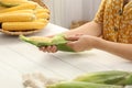 Woman husking corn cob at white wooden table, closeup