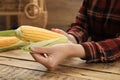 Woman husking corn cob at wooden table, closeup