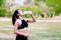 Woman hydrating post-workout in a park amidst greenery, embodying fitness and health. Teenage woman drinking water from a water Royalty Free Stock Photo