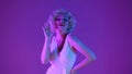 Woman in image of Marilyn Monroe in studio in pink and green neon light. The woman coquettishly waves her hand as a sign Royalty Free Stock Photo