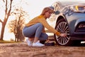 Woman Inflating Car Tyre With Electric Pump On Country Road