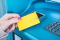 A woman is inserting a plastic yellow credit card into a blue ATM input device