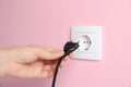 Woman inserting plug into power socket on pink wall, closeup. Electrical supply Royalty Free Stock Photo