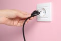 Woman inserting plug into power socket on pink wall, closeup. Electrical supply Royalty Free Stock Photo