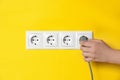 Woman inserting plug into power socket on yellow wall, closeup. Electrical supply Royalty Free Stock Photo