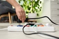 Woman inserting power plug into extension cord on floor indoors, closeup.