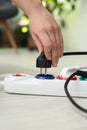 Woman inserting power plug into extension cord on floor indoors, closeup.