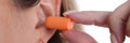 Woman inserts orange earplugs into ears closeup