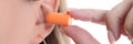 Woman inserts soft orange earplugs into ear closeup