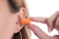 Woman inserts soft orange earplugs into ear closeup