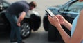 Woman insurance agent inspects damage to a man car and makes notes on a smartphone. Woman inspecting broken car Royalty Free Stock Photo