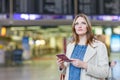 Woman at international airport, checking electronic board and waiting for her flight. Female passenger with european Royalty Free Stock Photo