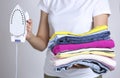 Woman with iron and stack of clothes in hands.Household.Clean folded colorful clothing
