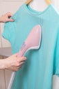 Woman ironing green shirt handheld garment steamer. Vertical steam irons brushes for ironing clothes generator Royalty Free Stock Photo