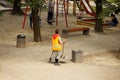 A woman janitor in orange overalls with a broom and dustpan stands on the street near the garbage bin. Cleaning of parks and