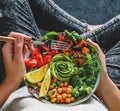 Woman in jeans holding Buddha bowl with salad, baked sweet potatoes, chickpeas, broccoli, greens, avocado, sprouts in hands. Royalty Free Stock Photo