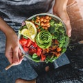 Woman in jeans holding Buddha bowl with salad, baked sweet potatoes, chickpeas, broccoli, greens, avocado, sprouts in hands. Royalty Free Stock Photo