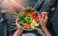 Woman in jeans holding Buddha bowl with salad, baked sweet potatoes, chickpeas, broccoli, greens, avocado, sprouts in hands. Royalty Free Stock Photo