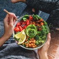 Woman in jeans holding Buddha bowl with salad, baked sweet potatoes, chickpeas, broccoli, greens, avocado, sprouts in hands. Royalty Free Stock Photo