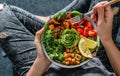 Woman in jeans holding Buddha bowl with salad, baked sweet potatoes, chickpeas, broccoli, greens, avocado, sprouts in hands. Royalty Free Stock Photo