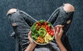 Woman in jeans holding Buddha bowl with salad, baked sweet potatoes, chickpeas, broccoli, greens, avocado, sprouts in hands. Royalty Free Stock Photo