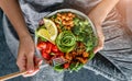 Woman in jeans holding Buddha bowl with salad, baked sweet potatoes, chickpeas, broccoli, greens, avocado, sprouts in hands. Royalty Free Stock Photo