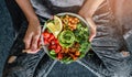 Woman in jeans holding Buddha bowl with salad, baked sweet potatoes, chickpeas, broccoli, greens, avocado, sprouts in hands. Royalty Free Stock Photo