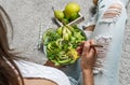 Woman in jeans holding fresh healthy greeen salad with avocado, kiwi, apple, cucumber, pear, greens and sesame on light background Royalty Free Stock Photo