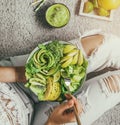 Woman in jeans holding fresh healthy greeen salad with avocado, kiwi, apple, cucumber, pear, greens and sesame on light background