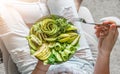 Woman in jeans holding fresh healthy greeen salad with avocado, kiwi, apple, cucumber, pear, greens and sesame on light background Royalty Free Stock Photo