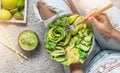 Woman in jeans holding fresh healthy greeen salad with avocado, kiwi, apple, cucumber, pear, greens and sesame on light background Royalty Free Stock Photo