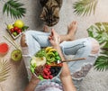 Woman in jeans holding fresh healthy green salad with quinoa, peach, avocado in bowl on light background with tropical leaves. Royalty Free Stock Photo