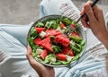 Woman in jeans holding fresh summer watermelon salad with feta cheese, arugula, spinach and greens on light background. Royalty Free Stock Photo