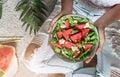 Woman in jeans holding fresh summer watermelon salad with feta cheese with smoothie on light background with tropical leaves. Royalty Free Stock Photo