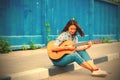 Woman in jeans sits on a road curb and plays the guitar Royalty Free Stock Photo