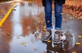 Woman in jeans and sneakers on a puddle of water at the middle of the road in autumn