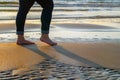 Woman in jeans walking on sandy beach at sunset. Close up of girl feet on the sand lit by golden sun light Royalty Free Stock Photo